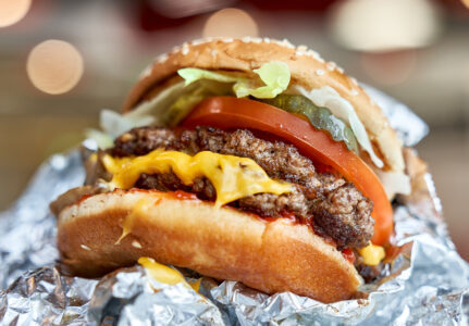 Five Guys cheeseburger partially wrapped in foil with lettuce and tomato.
