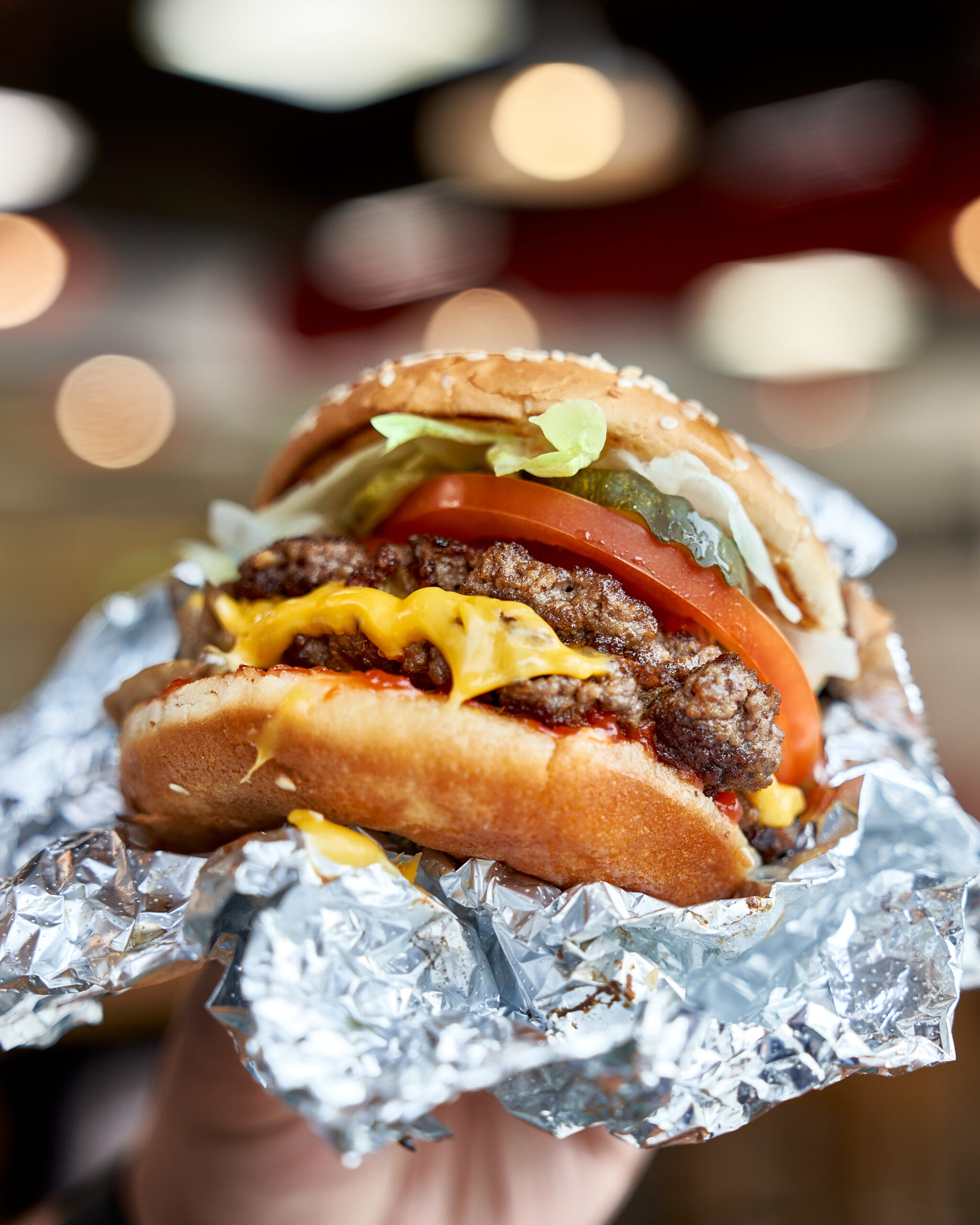 Cheeseburger wrapped in foil being held.