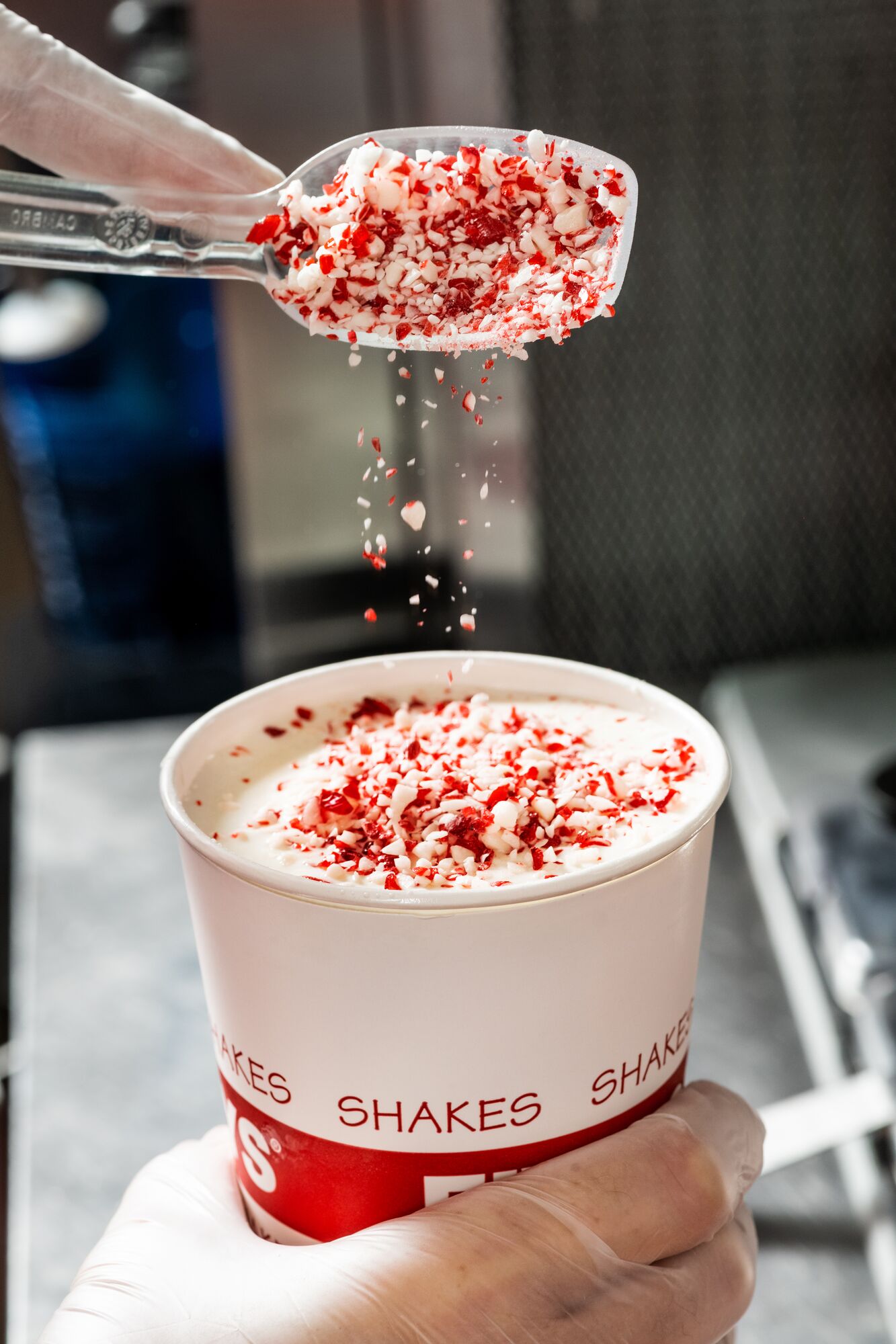 Scoop of Candy Cane Crunch being poured into a Five Guys milkshake.