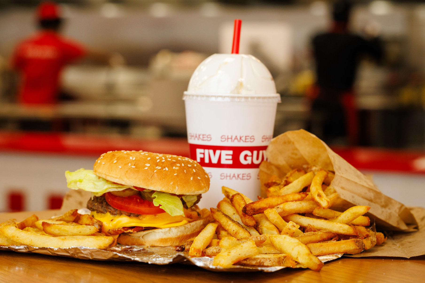 A Five Guys cheeseburger, milkshake and regular fry sit on a table inside a Five Guys restaurant.